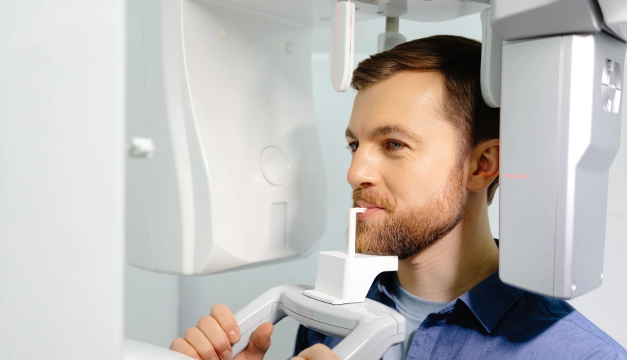 Male dentist in blue shirt examining digital dental X-ray on wall-mounted screen.