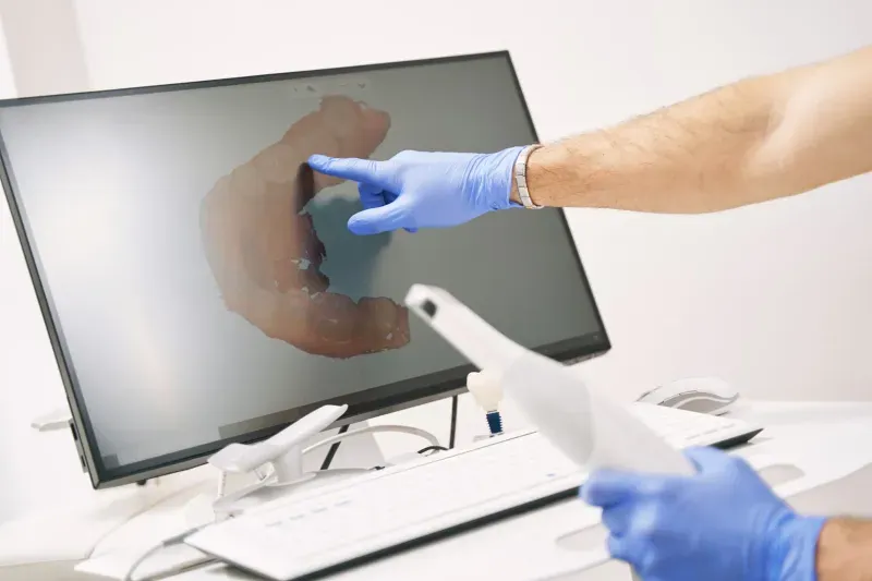 Person cleaning computer monitor screen with blue cloth and gloves in medical office setting.