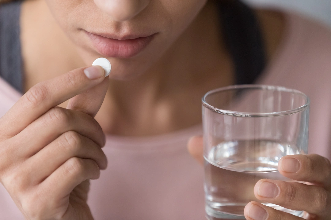 Woman holding pill with glass of water, about to take medication.